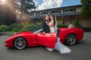 Groom seated on the back of a red convertible looking up at his bride in her ruffled gown