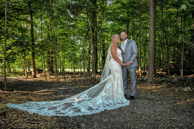 Bride and groom with a long trailing veil on the Maple Grove path at Forest Lodge