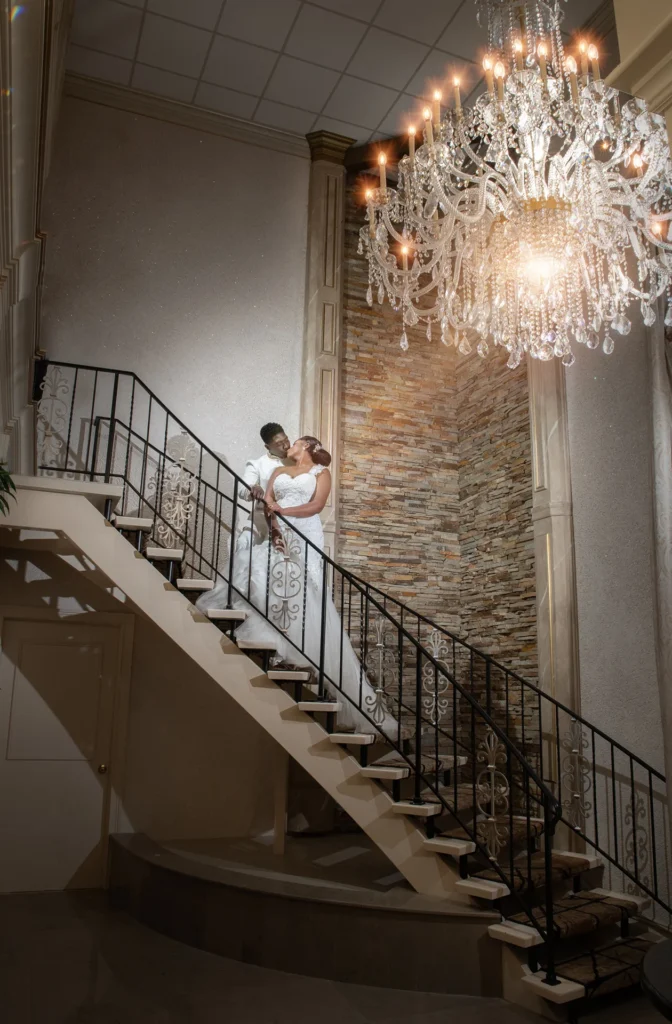 Bride and groom on the grand staircase beneath a chandelier at their Royal Manor wedding in Garfield, NJ