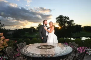 Couple embracing behind the mosaic fire pit table as the sun sets over the trees