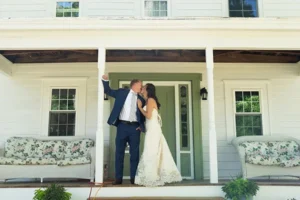 Groom raises his fist in celebration as he kisses his bride on the farmhouse front porch