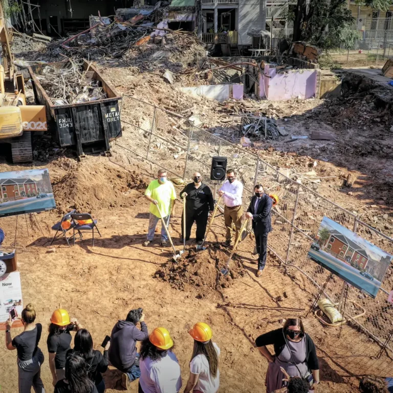 Overhead photo of a construction groundbreaking ceremony with officials in hard hats and press photographers